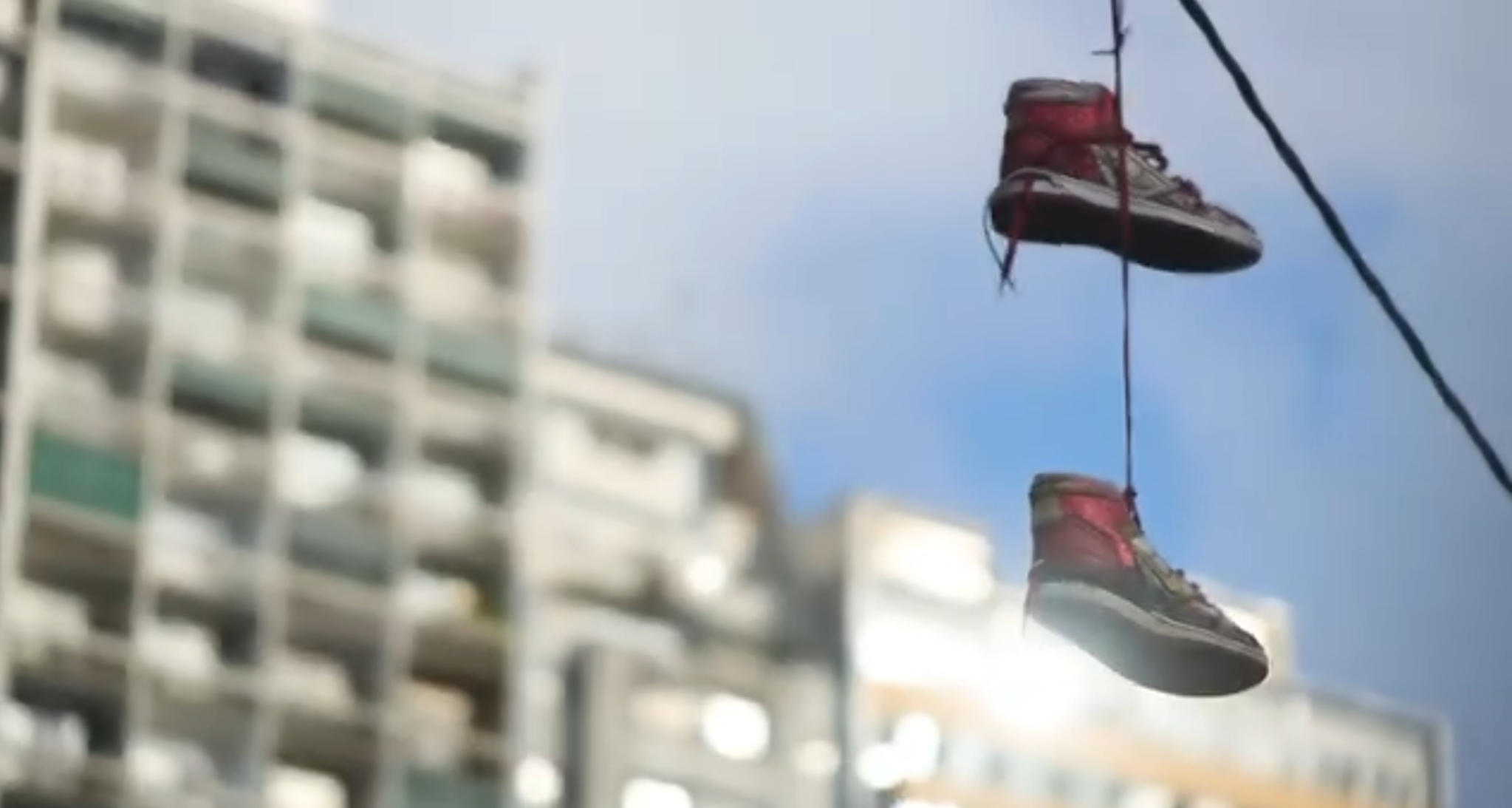 Dois tênis suspensos diante de edifícios, fotograma de Manobra